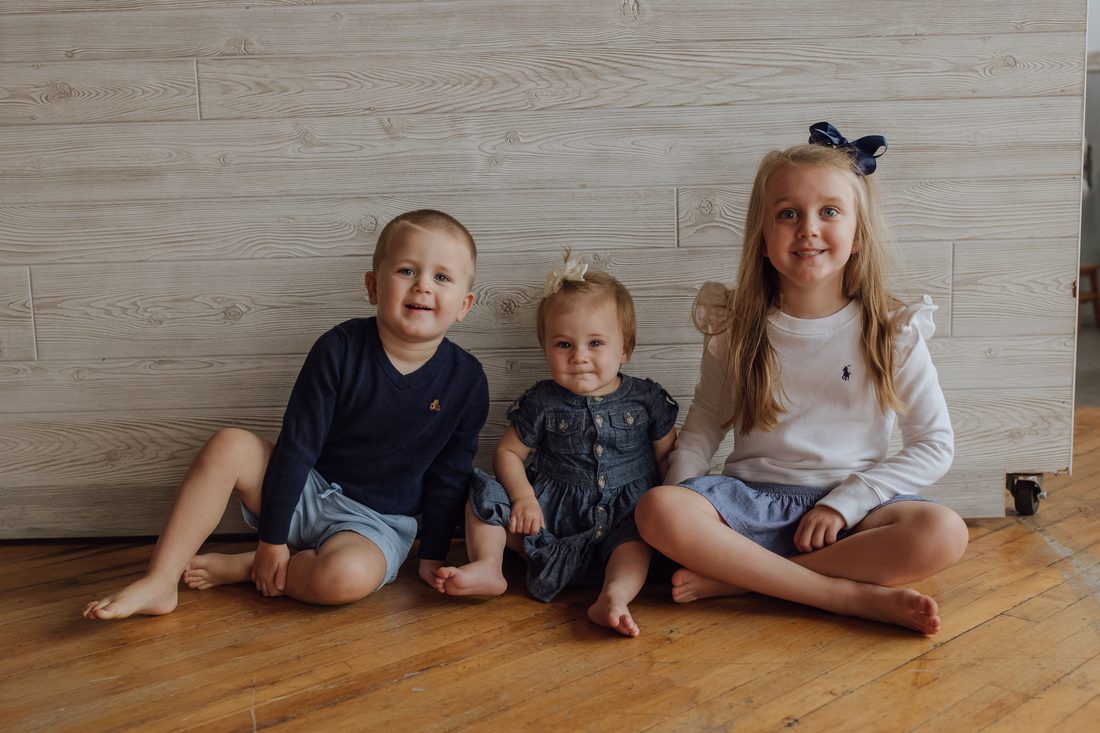The three Clark kids sitting against a whitewashed wood wall